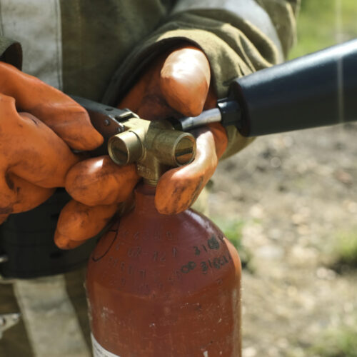 Close-up of firefighter with fire extinguisher. Clip. Firefighter picks up fire extinguisher and goes to extinguish fire. Firefighter in nature in summer